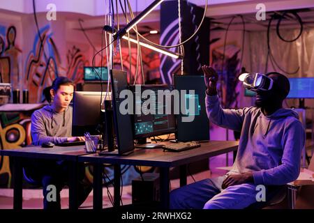 Hacker immersed in virtual reality metaverse while breaking into network system. Young criminal wearing vr headset while hacking online server and doing illegal activities at night time Stock Photo
