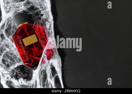 Bottle of elegant perfume with spiderweb for Halloween celebration on black background Stock Photo