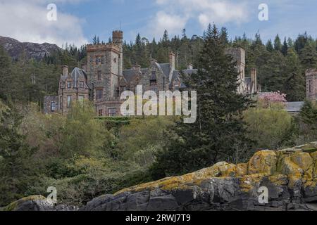 Loch Carron, Scotland, UK - May 1st 2023 - Renovated Scottish castle seen through the trees from a boat Stock Photo