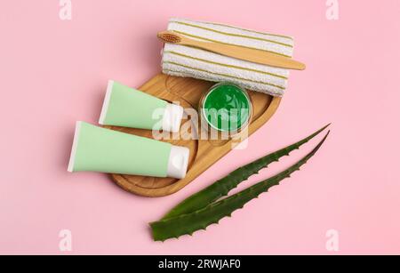 Tubes of toothpaste, fresh aloe, toothbrush and towel on pink background, flat lay Stock Photo