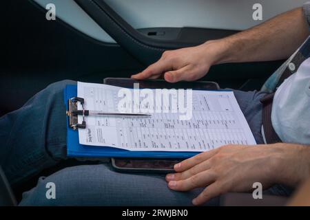 Male instructor sitting on the passenger seat with drive test report. Cropped view. Driving test, driver courses, exam concept Stock Photo