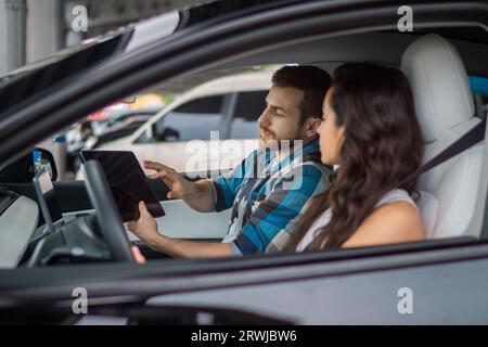 Male instructor holding digital tablet and explaining for woman during studying in drive school. Driving test, driver courses, exam concept Stock Photo