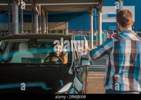 Male instructor showing thumbs up. Lady sitting inside car while passing exams successfully at driving school. Driving test, driver courses, exam Stock Photo