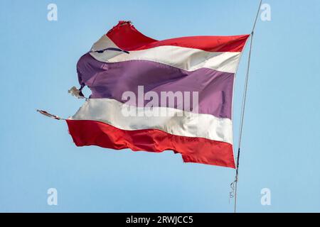 Torn national flag of Thailand flutters on a rope against a blue sky, Stock Photo