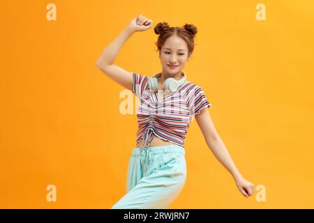 Girl dancing on yellow background wearing headphones on neck, lifestyle concept, copy space Stock Photo