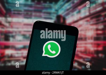 Whatsapp logo is displayed on a smartphone screen with a defocused red futuristic background Stock Photo