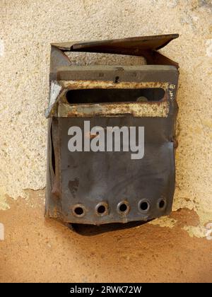 Old, somewhat rusty metal letterbox on a house wall on which the paint has already half peeled off Stock Photo