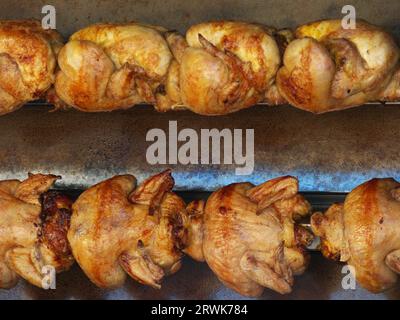 Several crispy brown chickens on a rotating grill, detail Stock Photo