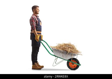 Full length profile shot of a farmer with hay in a wheelbarrow isolated on white background Stock Photo