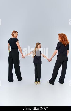 three generations, happy redhead family holding hands and standing in matching attire on grey Stock Photo