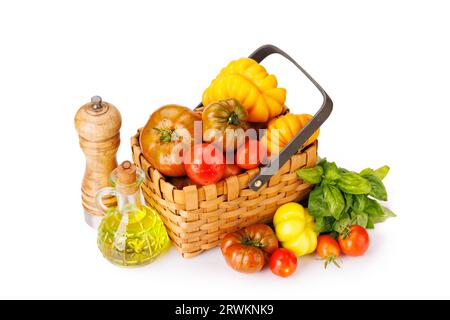 Assorted tomatoes in rustic basket, garden basil and spices. Isolated on white background Stock Photo