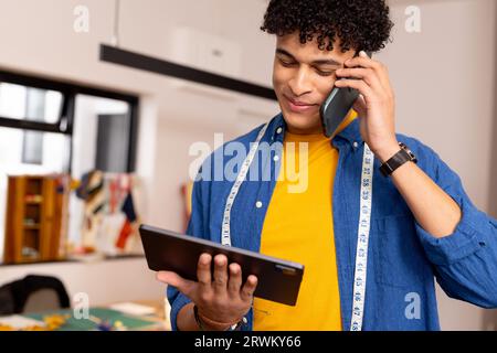 Happy biracial male fashion designer using tablet and smartphone in studio Stock Photo
