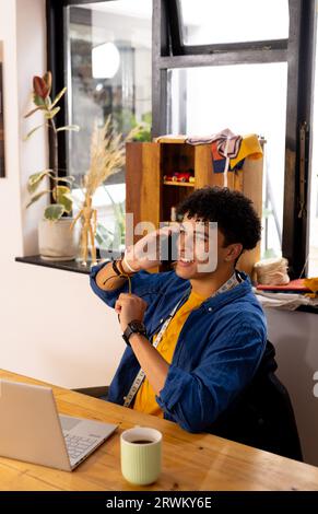 Smiling biracial male fashion designer using laptop and having call in studio Stock Photo