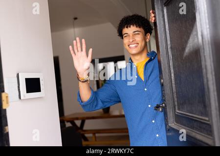 Happy biracial man standing, in doorway, smiling and waving Stock Photo