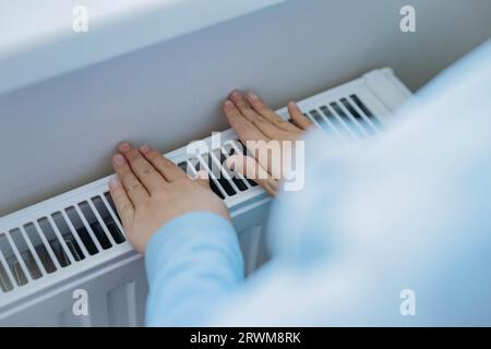 child warming hands over heater. Energy crisis in Europe. Image with selective focus Stock Photo