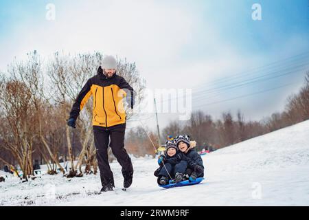 Dad ride his kids on sled in park. Winter activities. Happy family weekend on snowy day. Image with selective focus . High quality photo Stock Photo