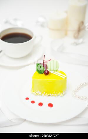 A cup of coffee with a heart-shaped cake in yellow glaze on a plate on a light background Stock Photo