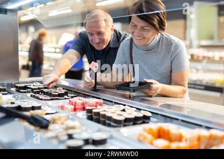 Couple chooses sushi near refrigerator in supermarket Stock Photo
