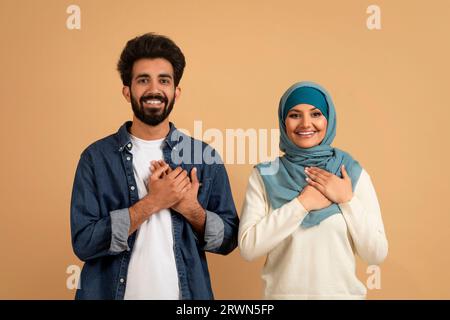 Grateful muslim couple keeping both hands on chest, expressing gratitude and appreciation Stock Photo