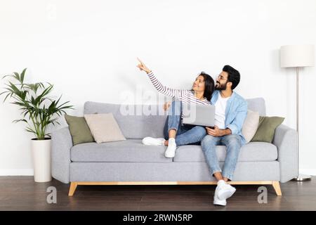Happy loving indian couple thinking on interior design, using laptop Stock Photo