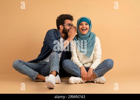 Sharing Secrets. Cheerful Arab Man Whispering Gossips To His Girlfriend's Ear Stock Photo