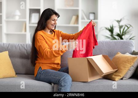 Excited young indian woman opening cardboard box parcel at home Stock Photo