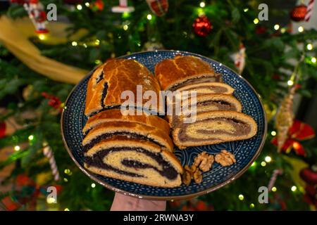 traditional hungarian christmas cookie calles bejgli filled with walnut and poppy seed with christmas tree background . Stock Photo