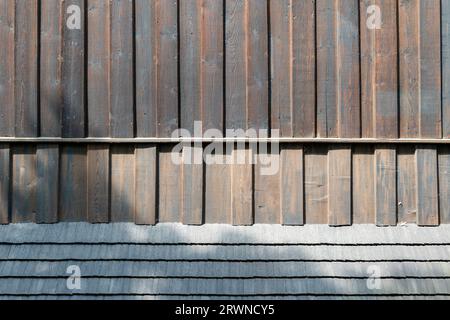 Detail of the facade of an old wooden church. Wooden boards and wooden shingles. The shadow from the trees is cast on the facades Stock Photo