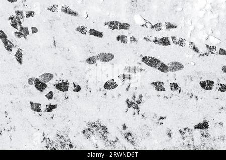 Black footprints over the snow on a gray asphalt road Stock Photo