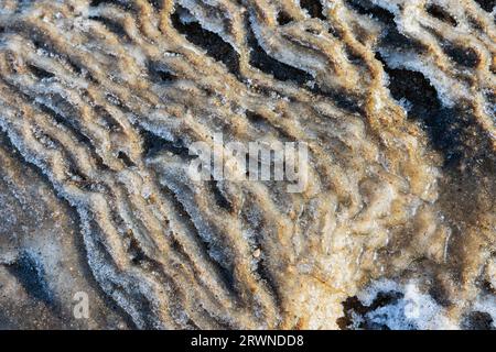 Abstract natural background photo with a wavy relief pattern of melting coastal ice mixed with snow and sand Stock Photo