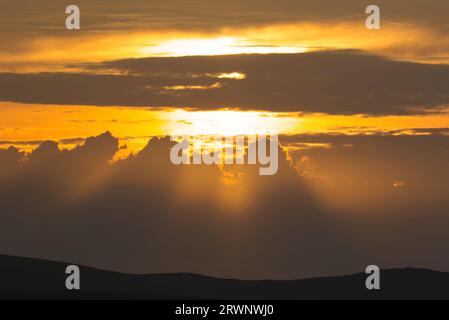 Orange glow of setting sun behind cloud Stock Photo