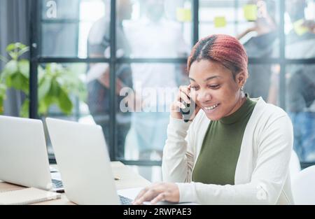 Mobile Communication Concept. Portrait Black Female Talking On Cellphone Working On Pc in Office Stock Photo