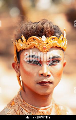 Close-up face of an Asian man in makeup with a golden crown on the head and golden necklace on his body while visiting the village Stock Photo