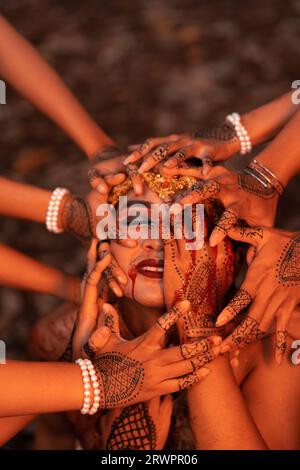 A Lot of hands holding an Asian man's face who had fake blood on her red lips like he was in pain in the forest Stock Photo