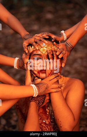 A Lot of hands holding an Asian man's face who had fake blood on her red lips like he was in pain in the forest Stock Photo