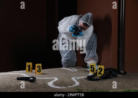 Criminologist in protective suit working at crime scene outdoors. Space for text Stock Photo