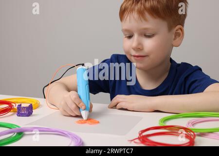 Boy drawing with stylish 3D pen at white table Stock Photo