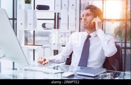 young web developer talking on phone while working with laptop in office Stock Photo