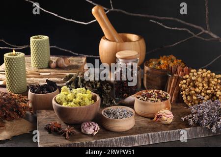 Many different dry herbs, mortar with pestle and candles on dark grey table Stock Photo