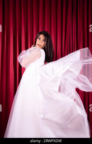 Beautiful Asian woman posing in a flying wedding dress in front of the red curtain in the studio Stock Photo