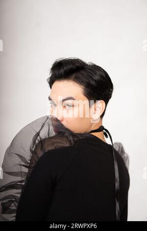 Asian man poses in a black costume while wearing makeup and black hair inside the studio Stock Photo