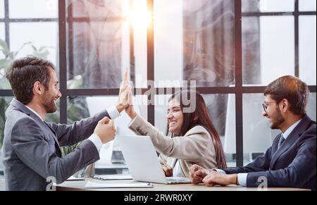 High five. Satisfied happy joyful employees have fun raising their right hands and sitting in the room next to their colleagues. Stock Photo