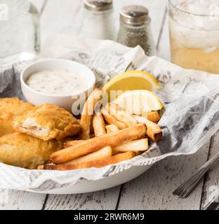 Fish and chips on newsprint designer parchment paper served with tartar sauce. Stock Photo