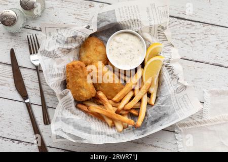 Fish and chips on newsprint designed parchment paper that is in soft focus. Stock Photo