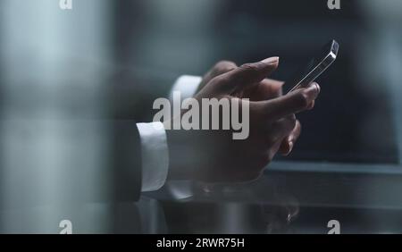 Close up cropped view of African male hands holding smartphone while sitting at table Stock Photo