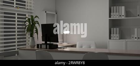 A modern white doctor's office or private office at night with a computer on a table, office supplies, a shelf, a window with window blinds, a table l Stock Photo