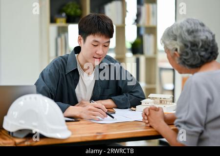 A professional Asian male engineer or architect is having a meeting with an old lady client about the house's building plan and process. Stock Photo