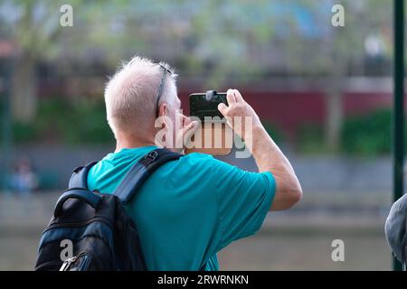 Senior man using smartphone to take photo outside wearing a backpack on a sunny day in Melbourne city, Australia. Stock Photo
