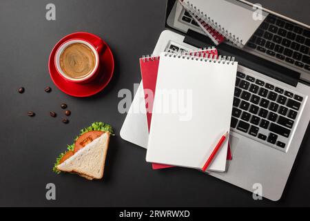 Blank notepad over laptop and coffee cup on office black table. Top view. Stock Photo