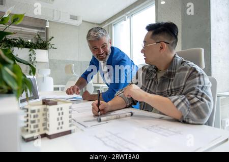 Two men architects using 3D printer in office and projecting house, drawing blueprints. Stock Photo